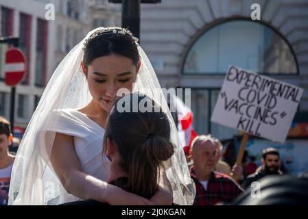 Protest taking place against vaccinating children for Covid 19, joined by anti-vaxxers, interrupting a wedding photoshoot with an Asian bride ignoring Stock Photo