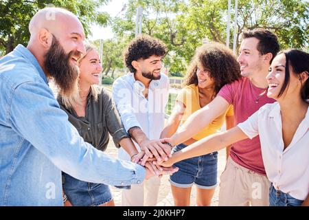 Group of people having fun together. Multiracial smiling friends stacking hands in a happy circle. Stock Photo