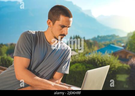 Young man working with laptop on beautiful scenic mountain background. Attractive man working. Freelancer. Traveler.  Stock Photo
