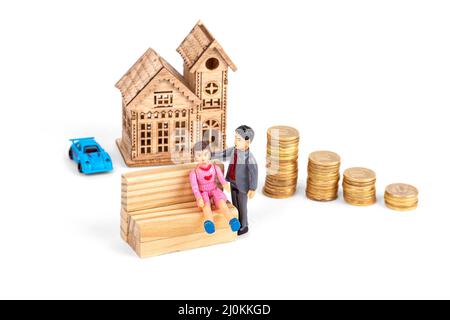 Toy figures of people, on the background of a wooden house and stacks of coins, on a white background Stock Photo