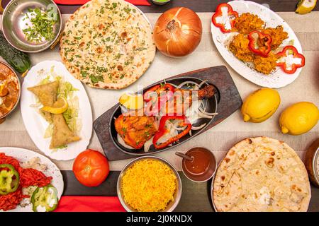 Set of Indian food dishes with hands dipping the chicken tikka masala, another into the stuffed samosas and curry and garlic naan and sauces Stock Photo