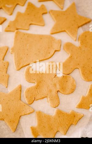 Process of making homemade cookies or gingerbread in different forms. Raw dough cookies lie on a baking sheet covered with parch Stock Photo