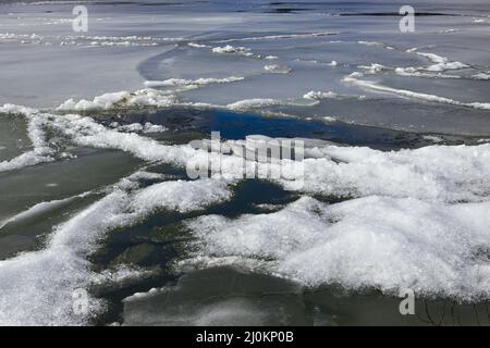 Snow is layered in clumps on a frozen yet slowly melting Hauser Lake in Idaho. Stock Photo