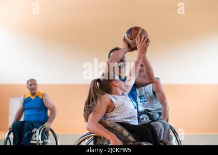 Disabled War veterans mixed race and age basketball teams in wheelchairs playing a training match in a sports gym hall. Handicap Stock Photo