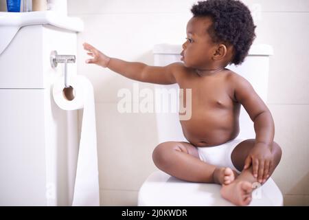 Potty training 101 Always make sure you have enough toilet paper. Shot of a baby boy sitting on the toilet and reaching for the toilet paper. Stock Photo