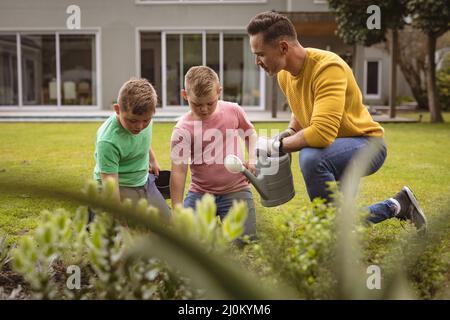 Caucasian father and two sons watering plants together in the garden Stock Photo