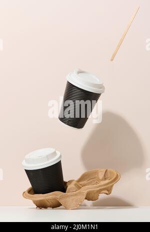 Two brown cardboard cups with a white plastic lid. Disposable tableware levitates against a beige background Stock Photo