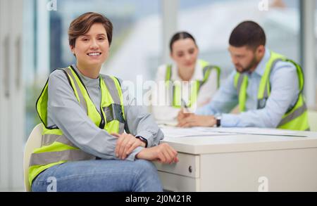 Weve got big plans. Cropped portrait of an attractive young female construction worker sitting in the boardroom with her colleagues in the background. Stock Photo
