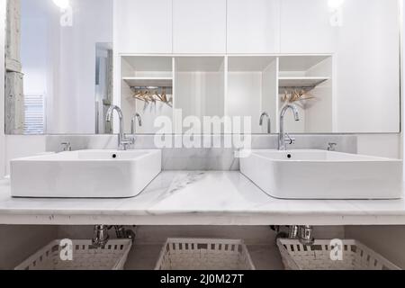 Bathroom decorated with twin porcelain sinks on white marble countertops and white painted wicker baskets Stock Photo