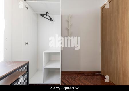 Open white wardrobe with shelving, clothes rail and black hangers Stock Photo