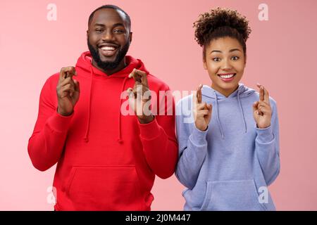 Lucky charming attractive positive african-american friends guy girl cross fingers making wish smiling broadly excited believe f Stock Photo