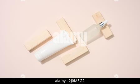 Plastic tube and white glass bottle with pipette stands on a beige background. Cosmetics SPA branding. Packaging for gel, serum, Stock Photo