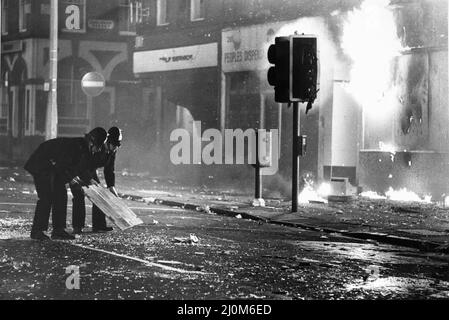 Toxteth Riot 6th July 1981Police officers try to clear broken glass from Park Road outside a burning looted shop, so the fire brigade can control the fire. The riots was sparked following the interception by police of motorcyclists Leroy Cooper in Selbourne Street. A crowd gathered, name-calling grew into jostling and within minutes there was a full-scale fracas that saw three police officers hurt and a young local man, arrested on assault charges. It did not stop there. Police mounted extra patrols in the area and early the following evening, July 4, they came under attack from a crowd armed Stock Photo