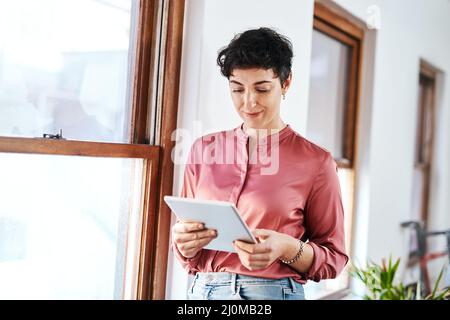 Checking company emails. Cropped shot of an attractive young businesswoman standing and using a tablet in her office alone. Stock Photo