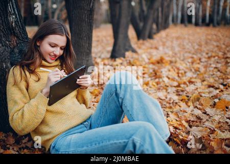 MOSCOW, RUSSIA - OCTOBER 19, 2021: Young woman model sitting with tablet Apple iPad Pro 2021 and painting with pencil stylus in Stock Photo