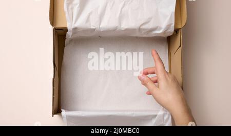Two female hands hold open paper box on a beige background, top view Stock Photo