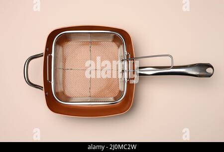 Empty copper deep frying pan with grill grate on beige background. View from above Stock Photo