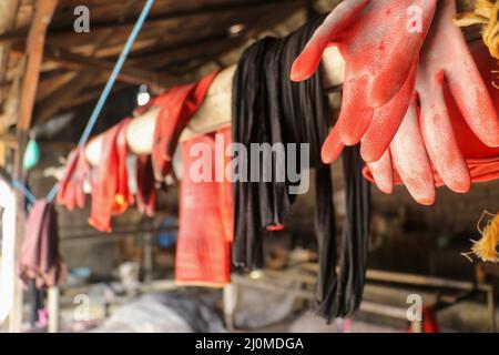 Background, blur, out of focus, bokeh. Red rubberized gloves hang in the bamboo stick. Drying rubber gloves Stock Photo
