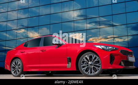Red car on a blue sky background with white clouds. A stylish, modern, bright image of an avto mobile for design solutions. Stock Photo