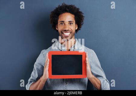 Special message just for you. Portrait of a happy young man holding up a small chalk board on a gray background. Stock Photo
