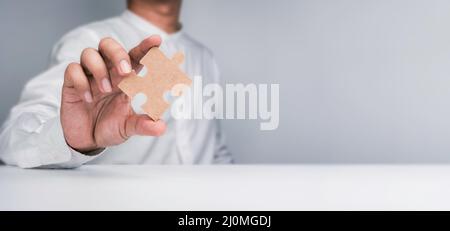 A one jigsaw puzzle element in a businessman's hand. Person hand showing a piece of the important jigsaw puzzle on the table and white background with Stock Photo