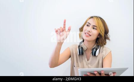 Music creation with digital device technology concept. Asian woman with short hair pointing or touch finger on virtual screen and using tablet with he Stock Photo