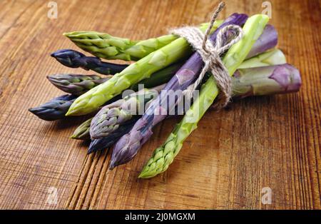 Raw green and violet asparagus bunch as close-up on rustic wooden board with copy space Stock Photo