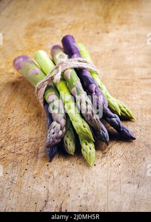 Raw green and violet asparagus bunch as close-up on rustic wooden board with copy space Stock Photo