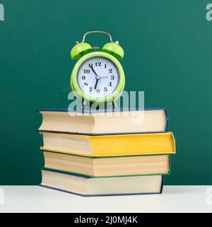 Round alarm clock and stack of books on empty chalk green board background Stock Photo