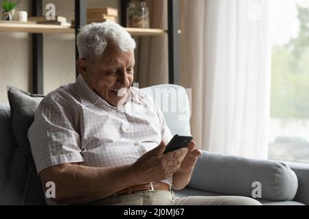 Smiling older grey-haired man using smartphone at home Stock Photo