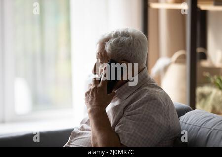 Elderly man holding smartphone talking sit on sofa at home Stock Photo