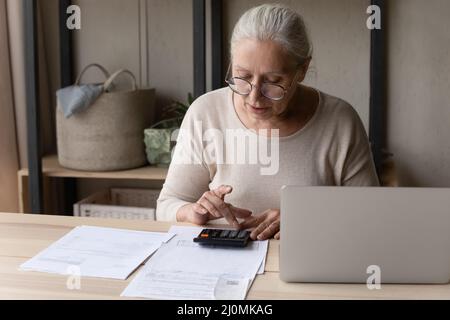 Older woman sitting at table using calculator manage personal budget Stock Photo