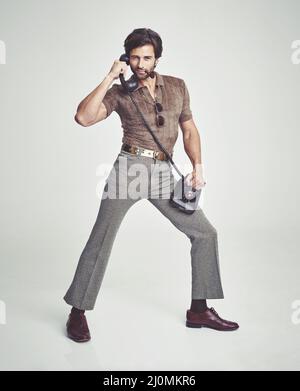 Doing everything with flair. A handsome man on a retro telephone while striking a pose. Stock Photo