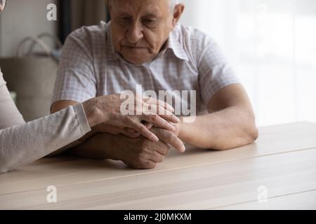 Upset senior man his wife holding hands seated at table Stock Photo