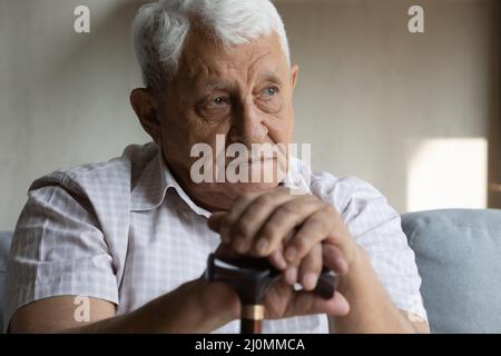 Older disabled man resting on couch hold cane looking upset Stock Photo