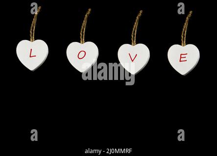 Four white wooden hearts with red text 'Love' on them. Black background. Stock Photo
