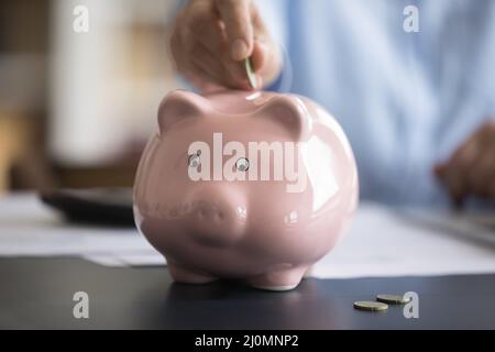 Close up cropped image female hand putting coin in piggybank Stock Photo