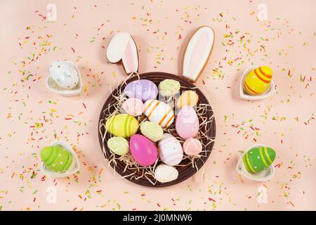 Gingerbread easter bunny ears and painted easter eggs on plate and sweet color sprinkles on a pastel background. Sweets for celebrating Easter. Stock Photo