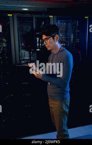 Asian male engineer writing on clipboard in computer server room Stock Photo