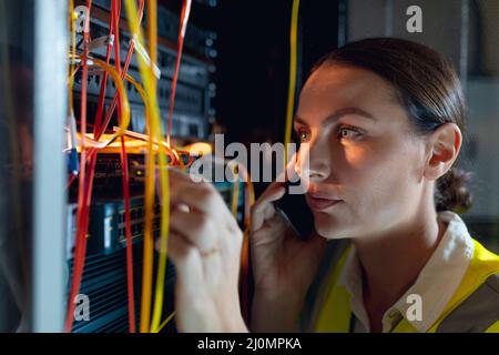 Close up of caucasian female engineer talking on smartphone while inspecting in computer server room Stock Photo