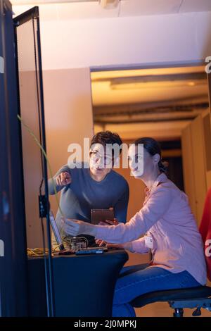Diverse male and female engineers discussing over a digital tablet while inspecting in server room Stock Photo