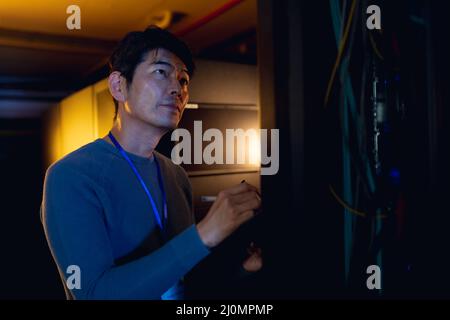 Asian male engineer writing on clipboard while inspecting in computer server room Stock Photo