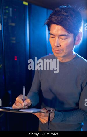 Asian male engineer writing on clipboard in computer server room Stock Photo