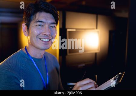 Portrait of asian male engineer smiling while writing on clipboard in computer server room Stock Photo
