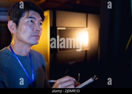 Asian male engineer writing on clipboard while inspecting in computer server room Stock Photo