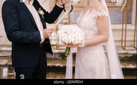 Groom with an umbrella in his hand reads an oath to the bride with a bouquet Stock Photo