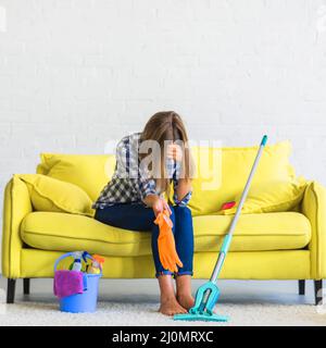 Frustrated young woman sitting sofa with cleaning equipments Stock Photo
