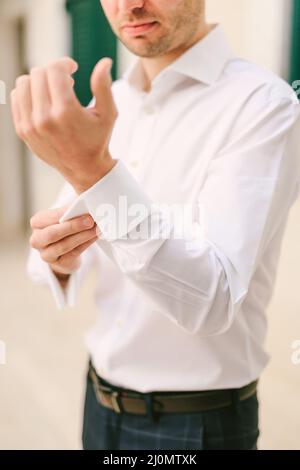 Man is buttoning the cuffs of a white shirt against the background of the wall. Close-up Stock Photo