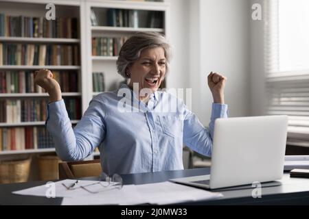 Happy older businesswoman feels excited reading good news on laptop Stock Photo