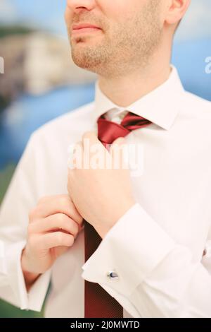 Man in a white shirt straightens his red tie with his hands. Close-up Stock Photo